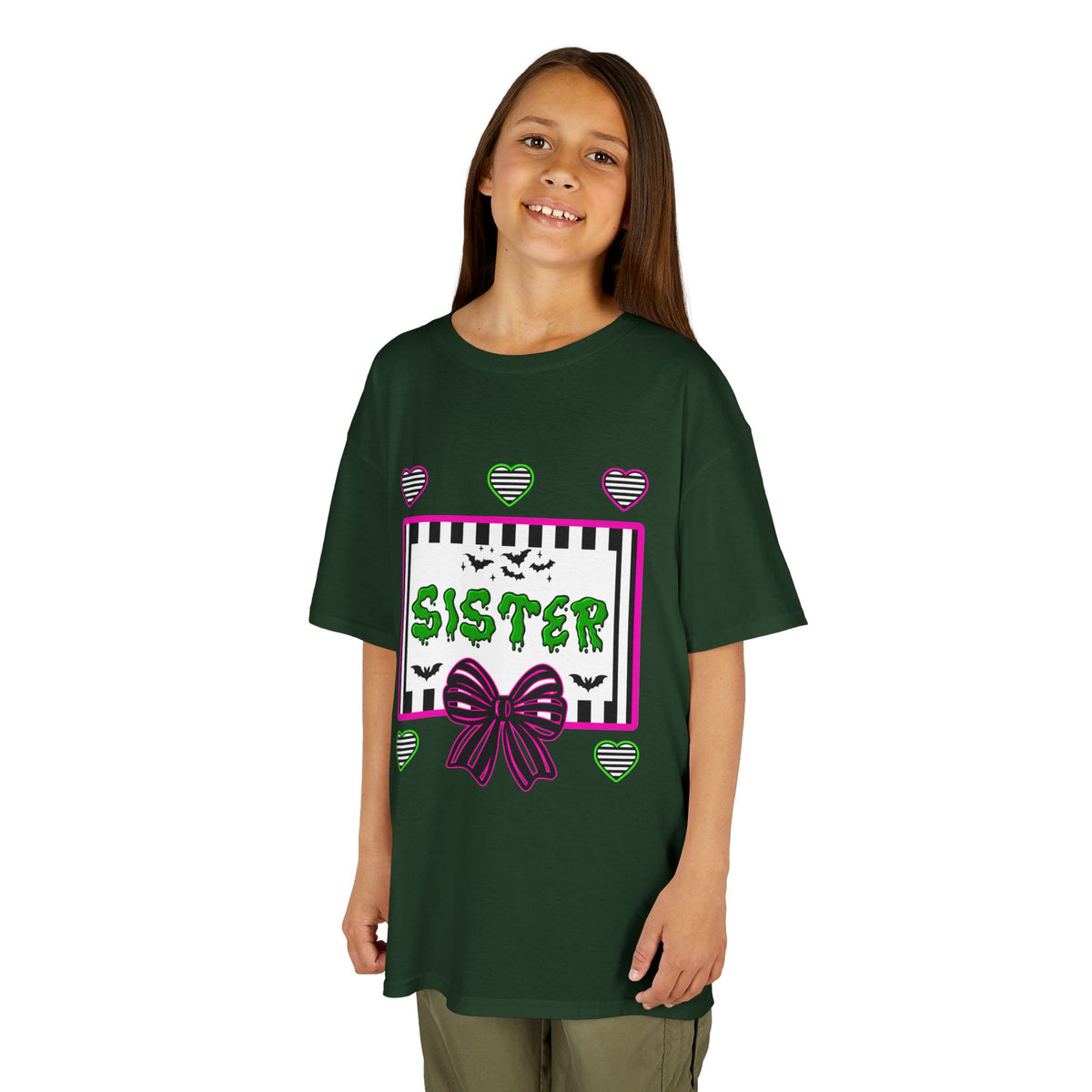 A young girl wearing a green t-shirt featuring a colorful Beetlejuice inspired Halloween-themed graphic with the word SISTER on the front. 