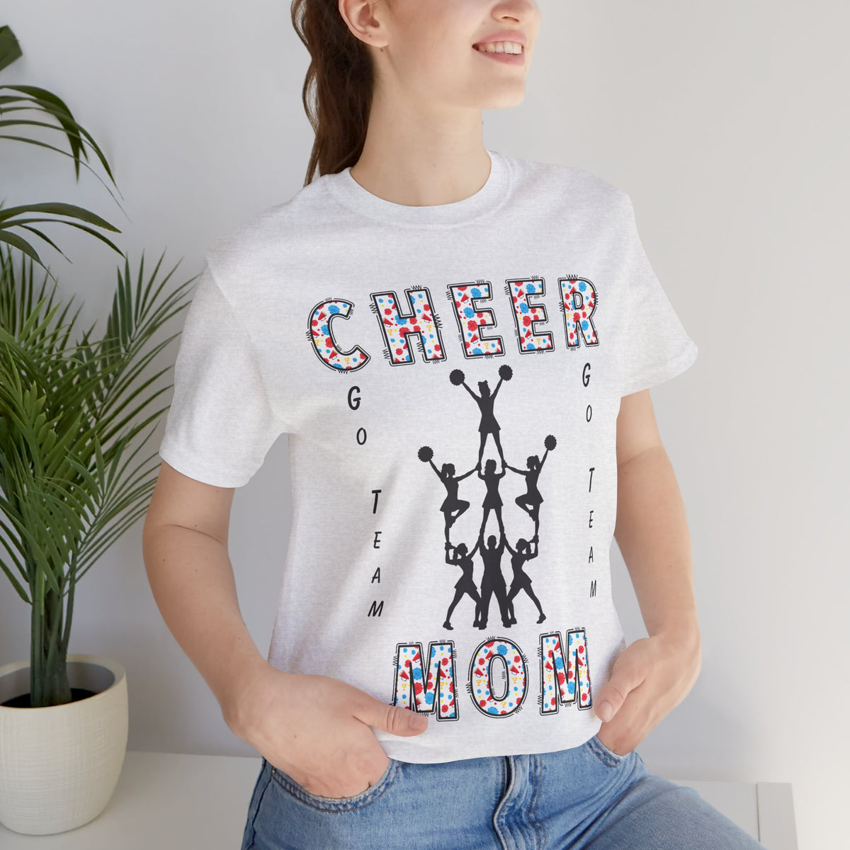 A woman wearing an ash colored graphic t-shirt with CHEER GO TEAM MOM text and graphic on the front.