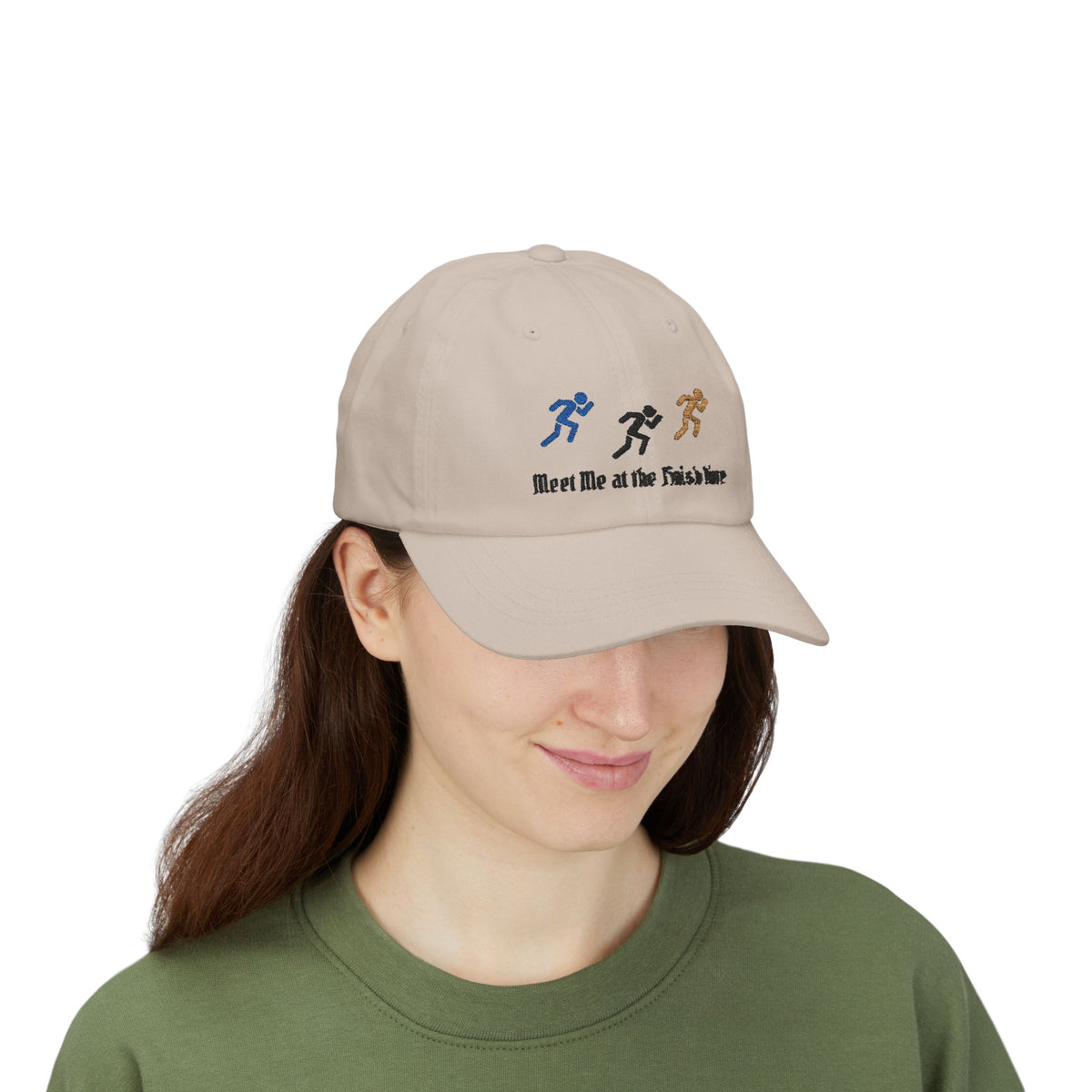 Woman wearing a stone baseball cap featuring embroidered running figures in blue, black, and tan above the text Meet Me at the Finish Line.