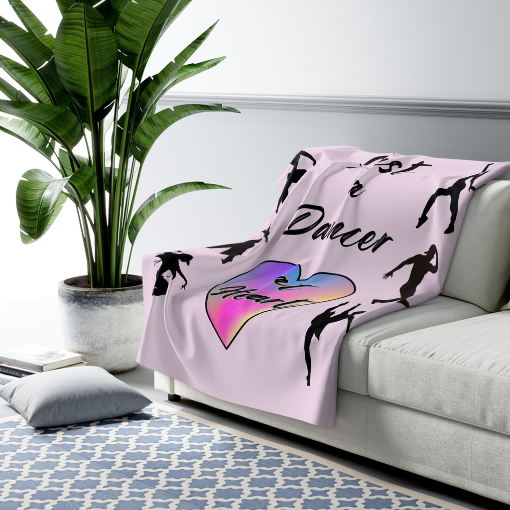 Pink sherpa fleece throw blanket featuring Just a Dancer at Heart text with heart and dancer graphics draped over a couch in a living room
