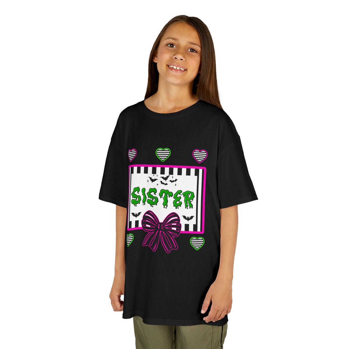 A young girl wearing a black t-shirt featuring a colorful Beetlejuice inspired Halloween-themed graphic with the word SISTER on the front. 