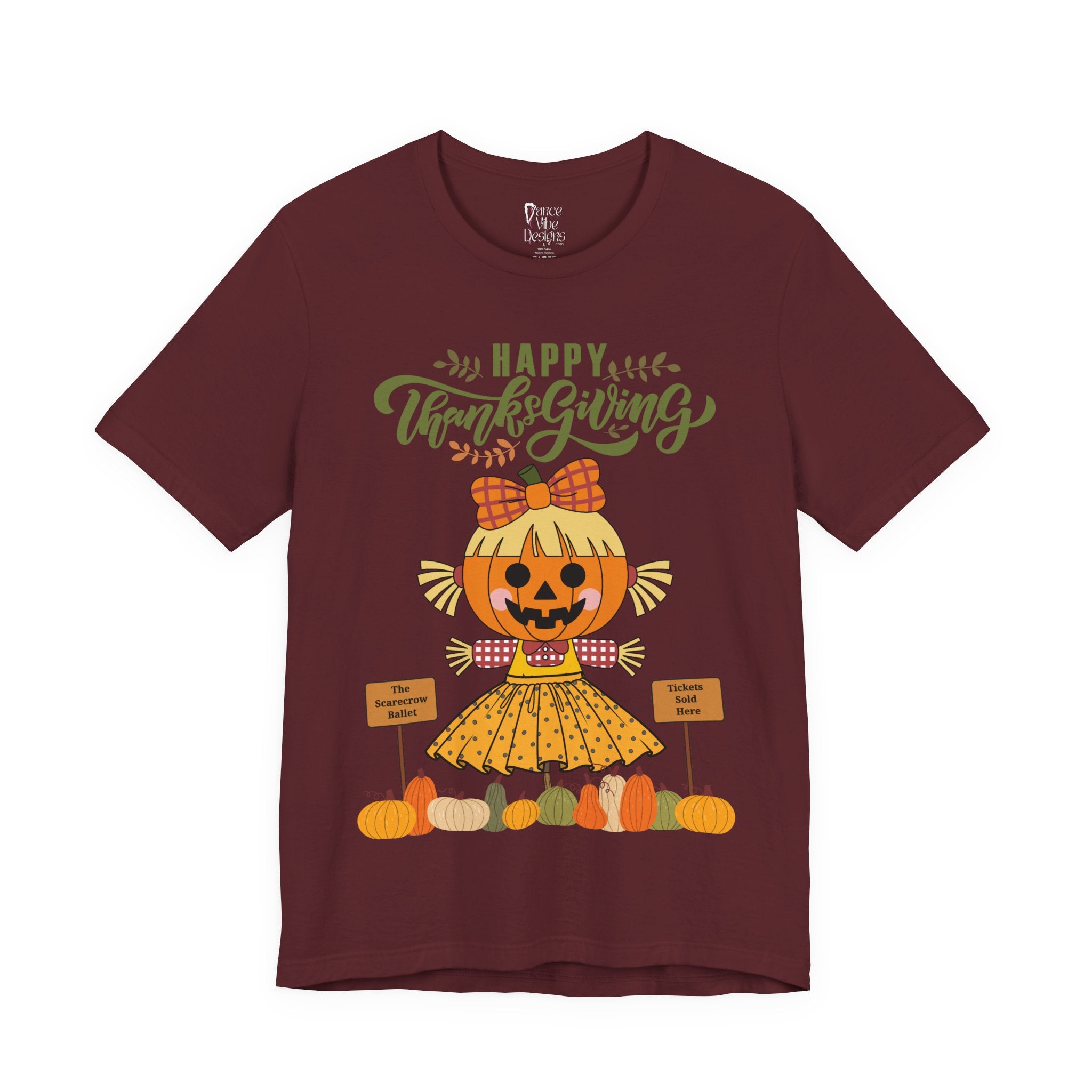 A maroon short-sleeve t-shirt with a Happy Thanksgiving graphic featuring a ballerina scarecrow design.