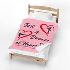 Pink velveteen plush throw blanket featuring Just a Dancer at Heart text with heart and ballerina graphics draped over a bed