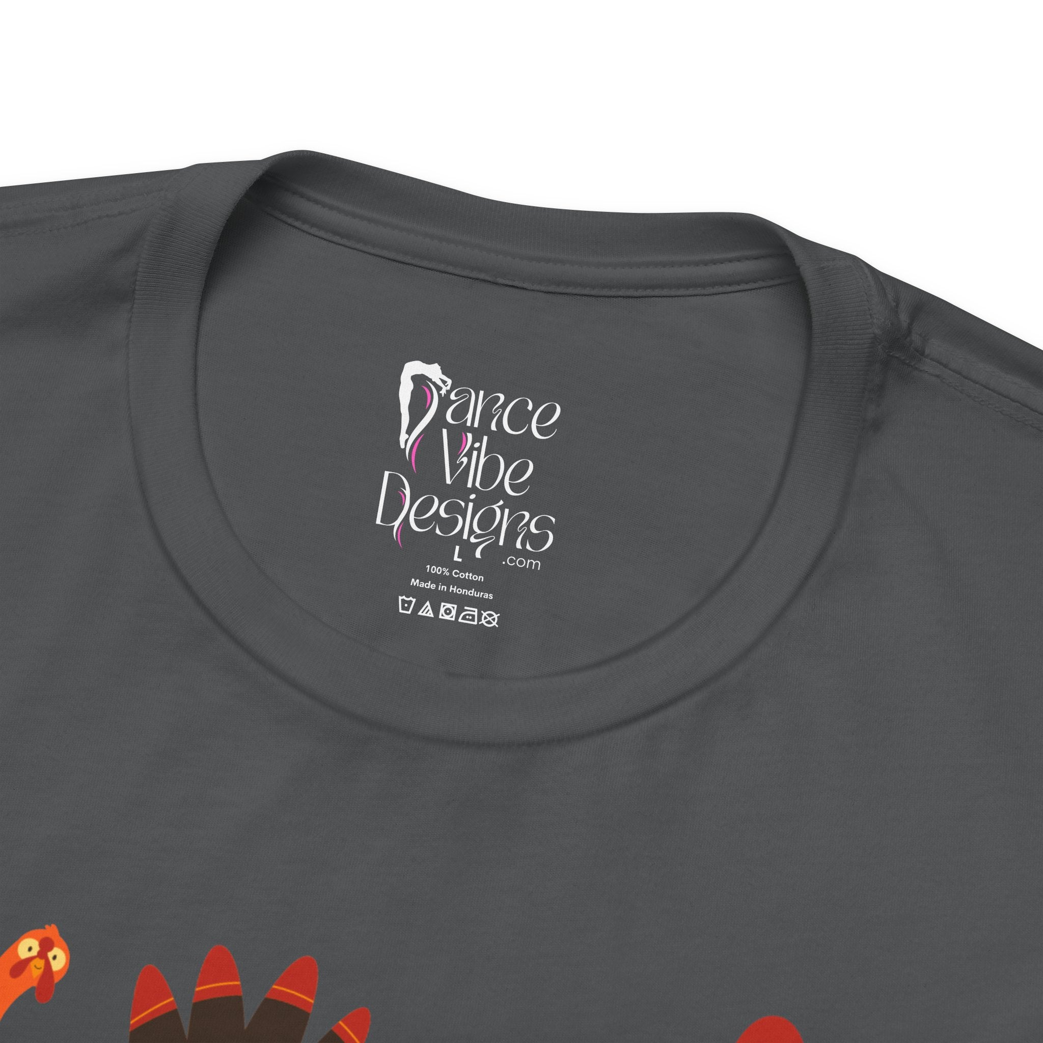 Close-up of a charcoal t-shirt showing the inner neck label with Dance Vibe Designs LLC printed in white, alongside care instructions.