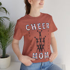 A woman wearing a heather clay graphic t-shirt with CHEER GO TEAM MOM text and graphic on the front.