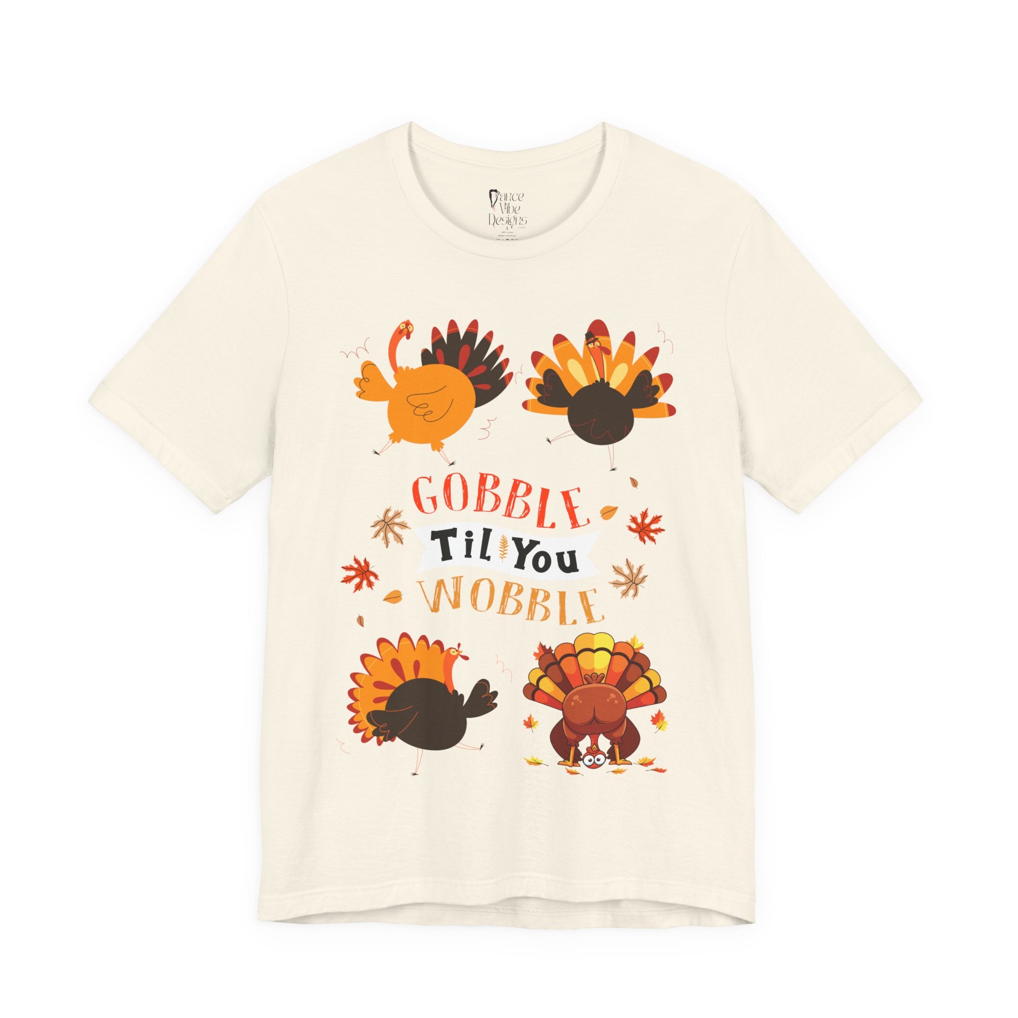 A natural short-sleeve t-shirt with a colorful Thanksgiving graphic featuring cartoon turkeys, autumn leaves, and the text GOBBLE Til You WOBBLE.