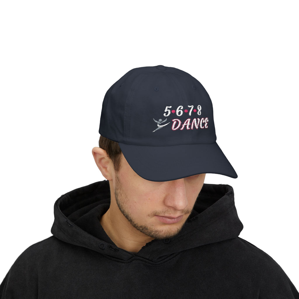A man wearing a navy baseball cap featuring the text 5-6-7-8 DANCE embroidered on the front, with a small dancer silhouette at the bottom.