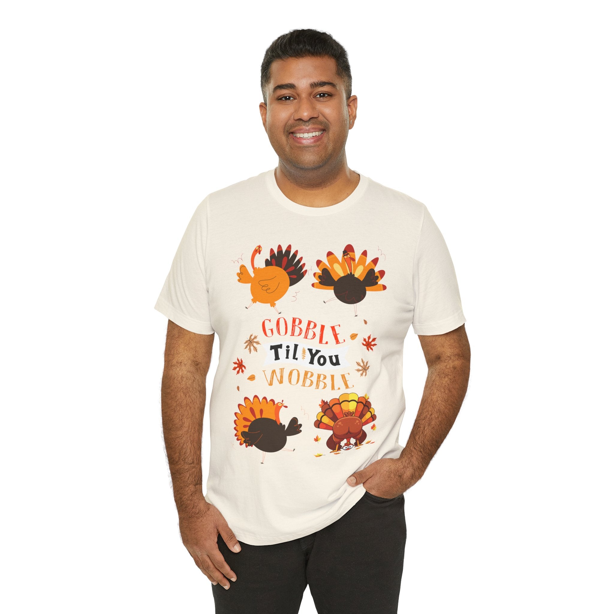 A man wearing a natural short-sleeve t-shirt with a colorful Thanksgiving graphic featuring cartoon turkeys and the text GOBBLE TIL YOU WOBBLE.