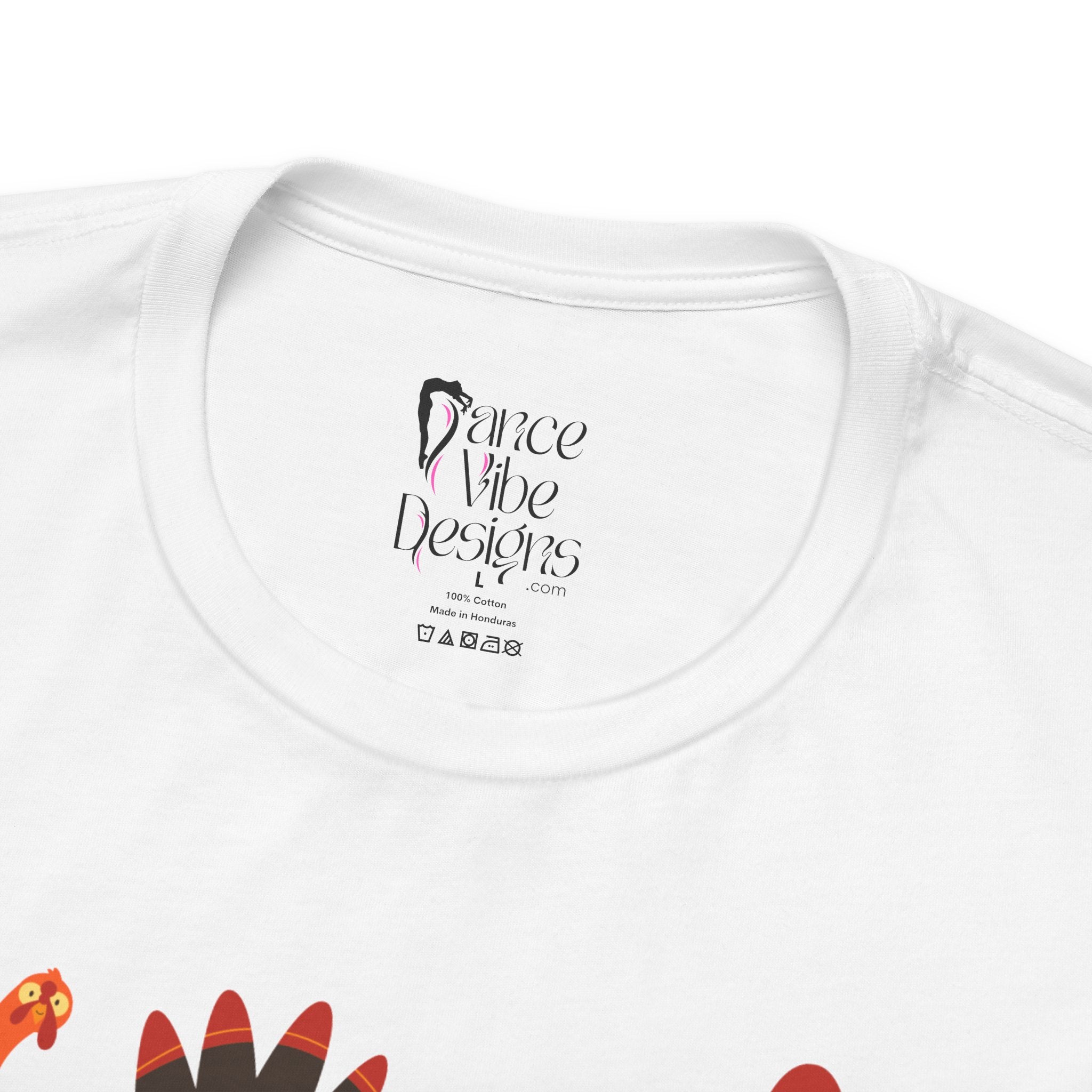 Close-up of a white t-shirt showing the inner neck label with Dance Vibe Designs LLC printed in black, alongside care instructions.