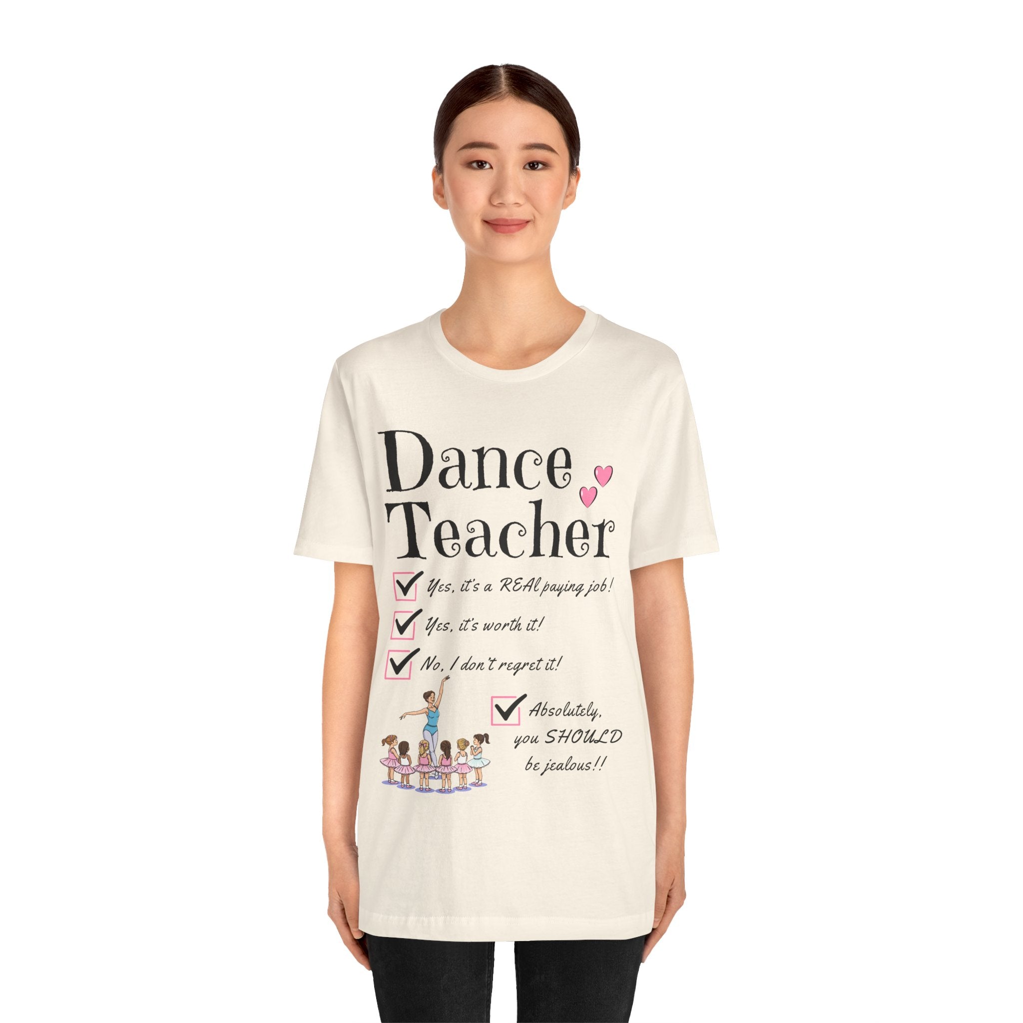 A young woman wearing a natural short-sleeve crewneck t-shirt featuring a text that reads Dance Teacher and a ballet class graphic.