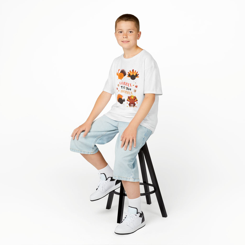Young boy wearing a white short-sleeve t-shirt with a colorful graphic of cartoon turkeys and the phrase GOBBLE TIL YOU WOBBLE on the front.