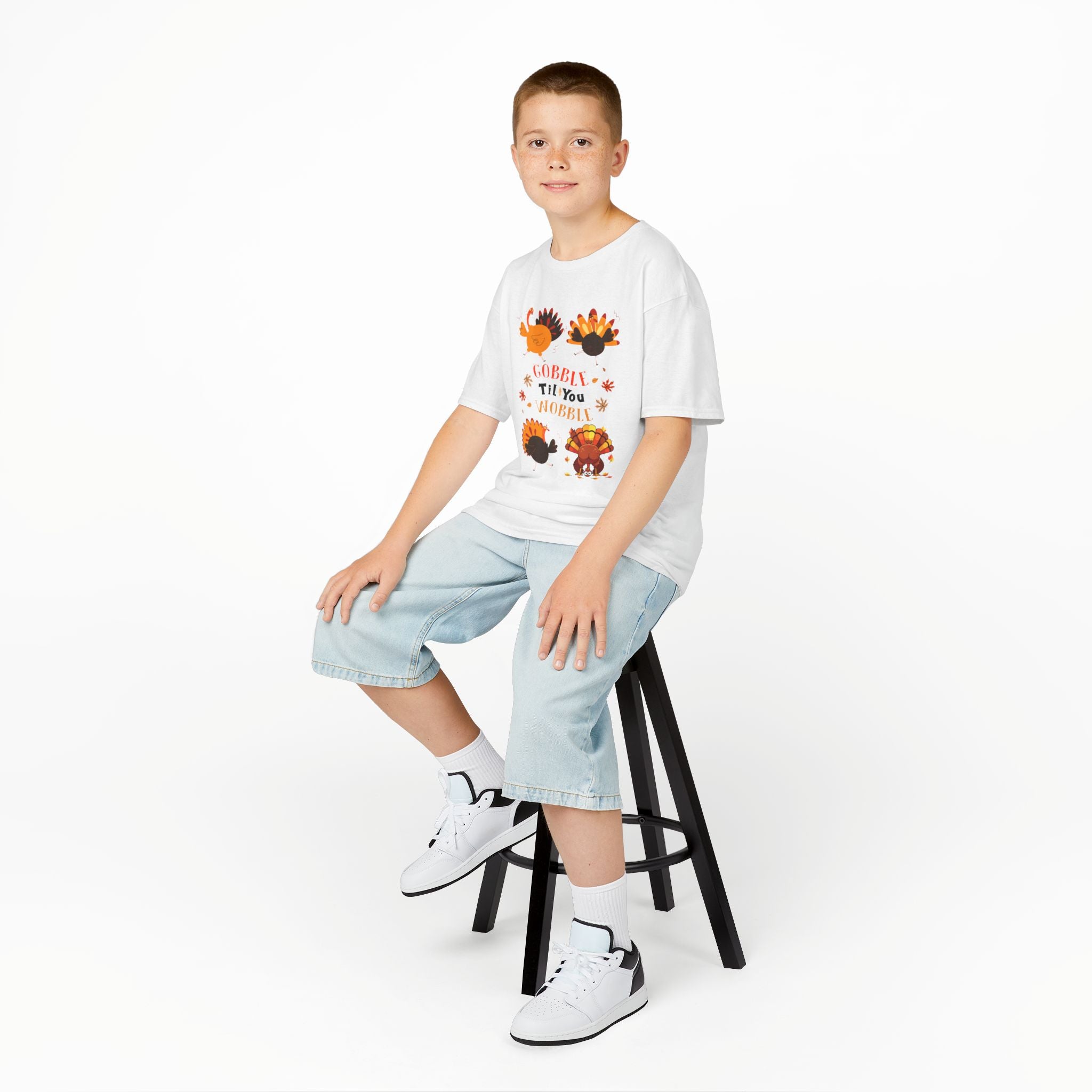Young boy wearing a white short-sleeve t-shirt with a colorful graphic of cartoon turkeys and the phrase GOBBLE TIL YOU WOBBLE on the front.