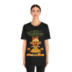 A woman wearing a black short-sleeve t-shirt with a Happy Thanksgiving graphic featuring a ballerina scarecrow design.