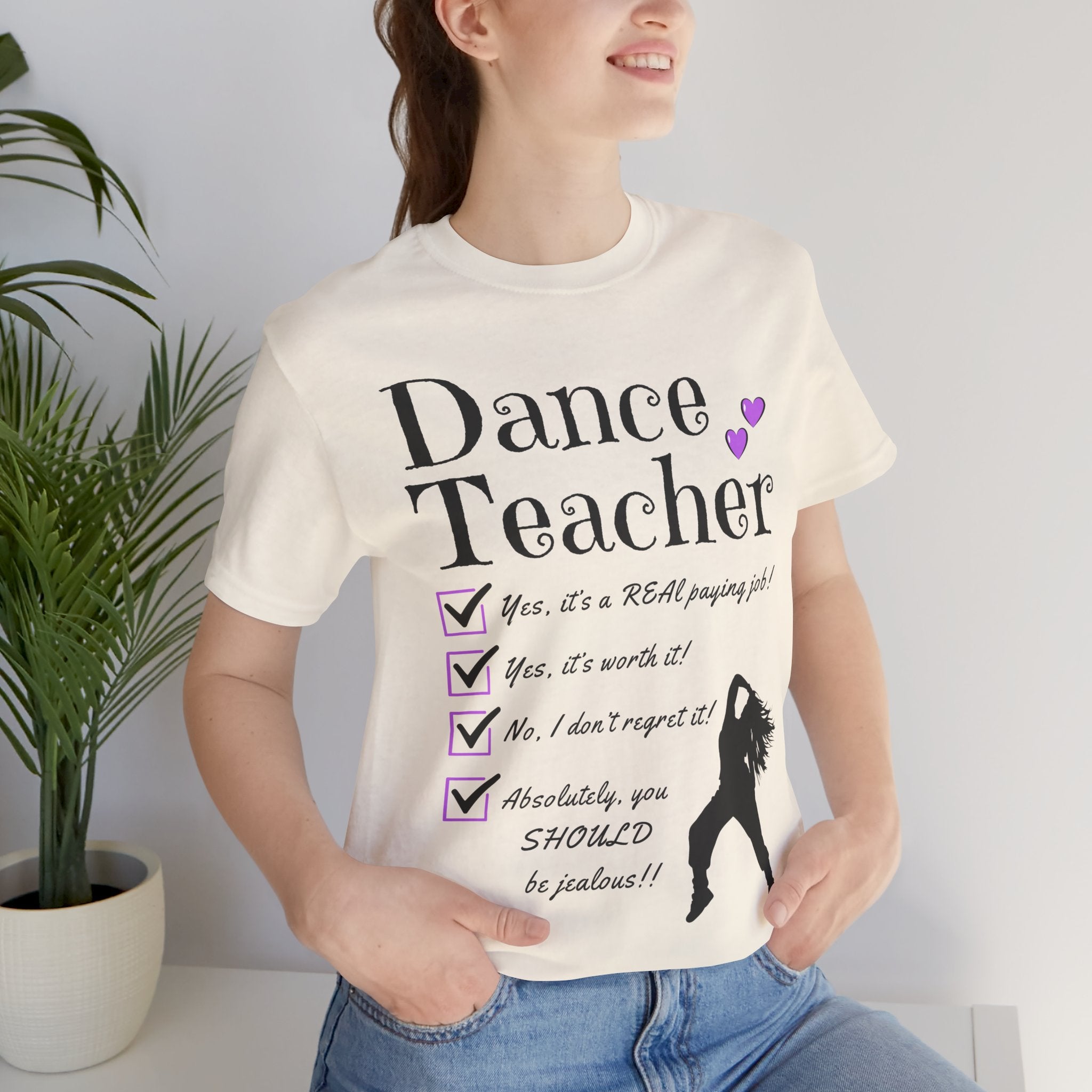 Woman wearing a natural short-sleeve graphic t-shirt featuring the text Dance Teacher with a jazz, hip hop dancer silhouette.