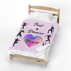 Pink velveteen plush throw blanket with dancer silhouettes a rainbow heart and Just a Dancer at Heart text covering a bed