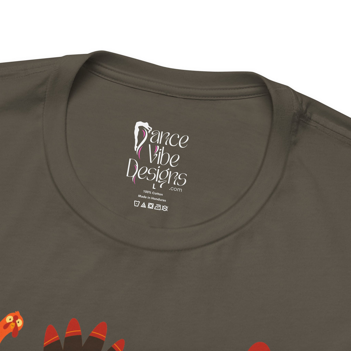 Close-up of an army green t-shirt showing the inner neck label with Dance Vibe Designs LLC printed in white, alongside care instructions.