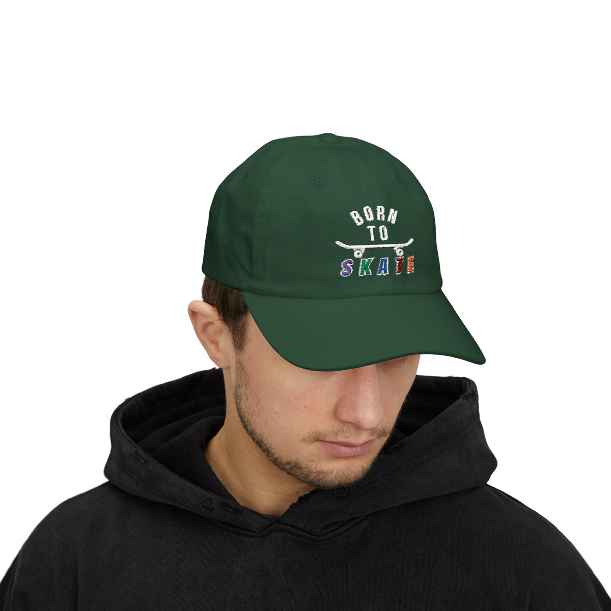 Man wearing a spruce baseball cap featuring a graphic on the front that reads BORN TO SKATE with a skateboard illustration. 