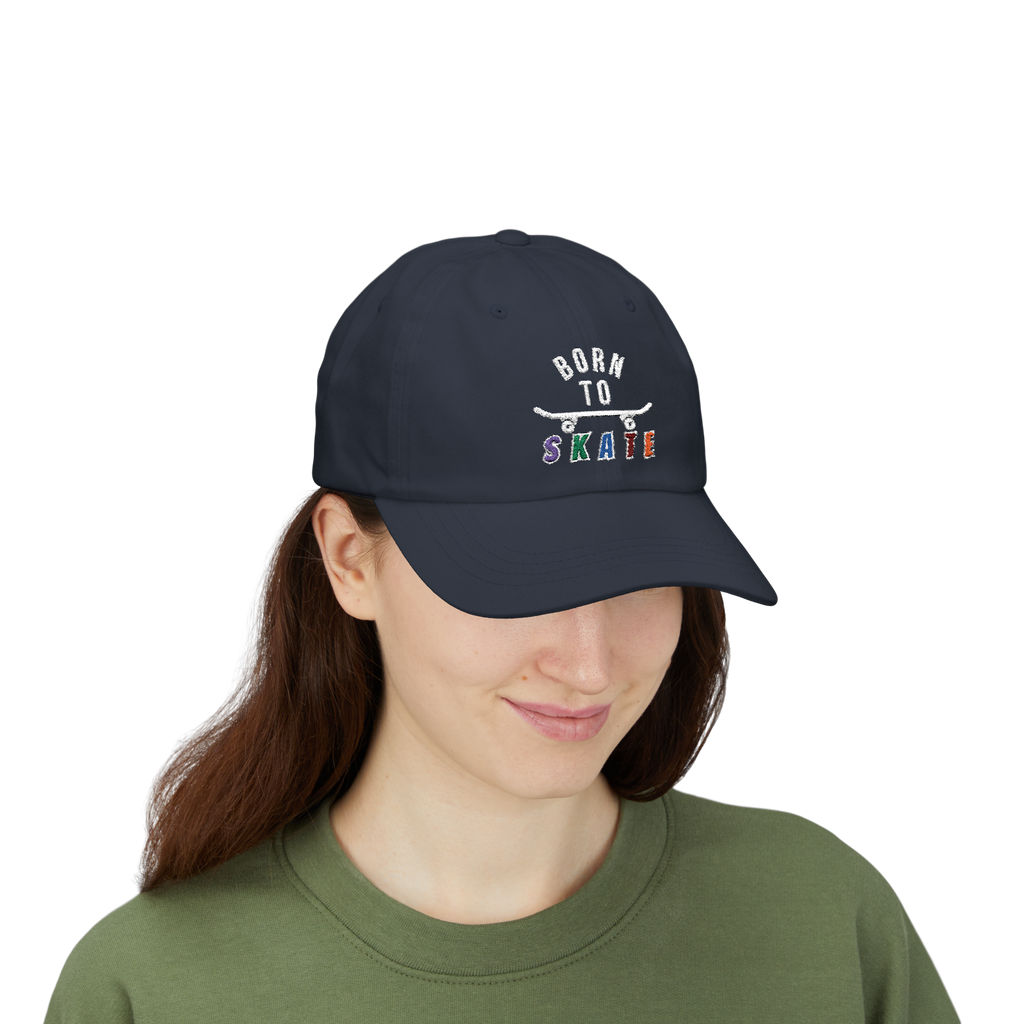 A woman wearing a navy baseball cap featuring a graphic on the front that reads BORN TO SKATE with a skateboard illustration. 